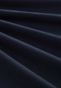 Tissu bleu marine foncé avec une texture lisse, présentant de profonds plis qui créent des ombres. Le matériau semble léger et durable.
