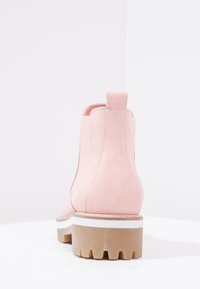 Różowe zamszowe botki za kostkę z elastycznymi bokami, białą paskiem wzdłuż podeszwy, teksturowaną gumową podeszwą oraz pętelką z tyłu.