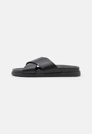 Sandale noire en cuir lisse avec des brides croisées. Dotée d'une semelle plate et texturée pour le confort et la durabilité.