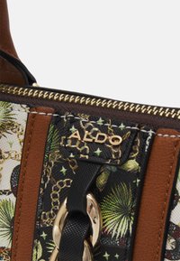 Multi-colored handbag featuring a floral pattern, leather accents in brown, gold-toned hardware, and a zip closure with contrasting stitching details.