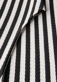 Texturerat tyg med växlande svarta och vita ränder i ett mönster. Materialet verkar vävt med en lätt stretch.