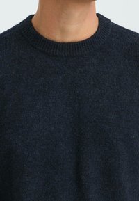 Marineblauer Wollpullover mit einem gerippten Rundhalsausschnitt und einer weichen, strukturierten Oberfläche. Nahaufnahme, die die Stoffdetails hervorgehoben zeigt.