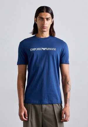 Tricou din bumbac de culoare bleumarin, cu un logo imprimat "Emporio Armani" pe piept, design cu guler rotund și mâneci scurte.