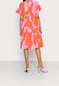 Vestido colorido con grandes patrones abstractos en rosa y naranja, mangas cortas con volantes y una falda en capas con un detalle de ojal en la parte trasera.