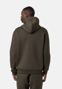 Hoodie verde oliva con cappuccio regolabile, polsini e orlo a coste. Texture liscia, design minimal. Indossato con pantaloni jogger abbinati.