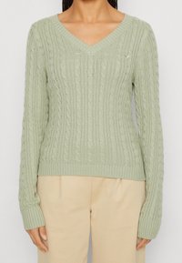 Hellgrüner Strickpullover mit V-Ausschnitt und einem Zopfmuster. Mit gerippten Bündchen und Saum, aus einem weichen Textil gefertigt.