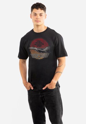 Black cotton t-shirt featuring a graphic print of a jet with text, "I FEEL THE NEED...THE NEED FOR SPEED!" and “TOP GUN” in red and gray.
