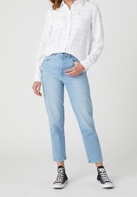 Ljusblå högmidjade jeans med rakt ben, tillsammans med en vit långärmad skjorta med knappar och två bröstfickor. Svarta högskurna sneakers.