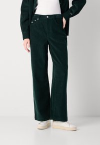 Grüne Corduroy-Hosen mit weitem Bein und strukturiertem Finish, ausgestattet mit Fronttaschen, einem Knopfverschluss und einem kleinen Logo am Bund.