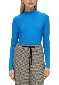 Dlhý rukáv rolák v jasnej modrej farbe, vyrobený z hladkej látky, kombinovaný s vysoko pásmi nohavicami s čierno-bielym vzorom houndstooth.