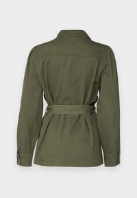 Oliwkowa kurtka z paskiem, wykonana z bawełny, z długimi rękawami, kołnierzykiem i zaszewkami na plecach, które nadają kształt. Gładka tekstura z ozdobnymi guzikami na mankietach.