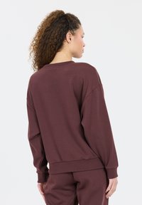 Burgunderfarbener Sweatshirt mit langen Ärmeln und gerippten Manschetten, mit Rundhalsausschnitt und minimalem Branding auf der Rückseite in Nackenhöhe.