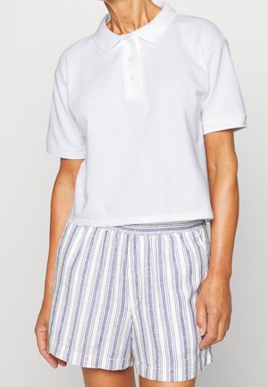 Valkoinen puuvillainen poolopaita, jossa kaulus ja kolmen napin aukko, yhdistetty vaaleansiniraidallisiin shortseihin, joissa on joustava vyötärö.