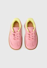 Roze antilopne tenisice s žutim podstavljenim ovratnikom, gumeni đon, vezice i Puma branding, prikazane odozgo na bijeloj pozadini.