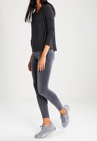 Mörkgrå långärmad topp, slim-fit grå leggings och ljusgrå träningsskor. Bekväm tyg, avslappnad design och ankellång stil.
