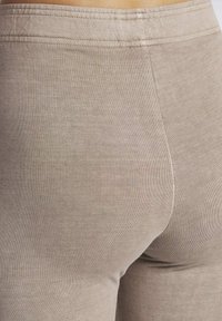 Beżowe legginsy wykonane z miękkiego, elastycznego materiału, z prążkowaną teksturą i dopasowanym krojem. Szwy są starannie wykończone, co zapewnia schludny wygląd.