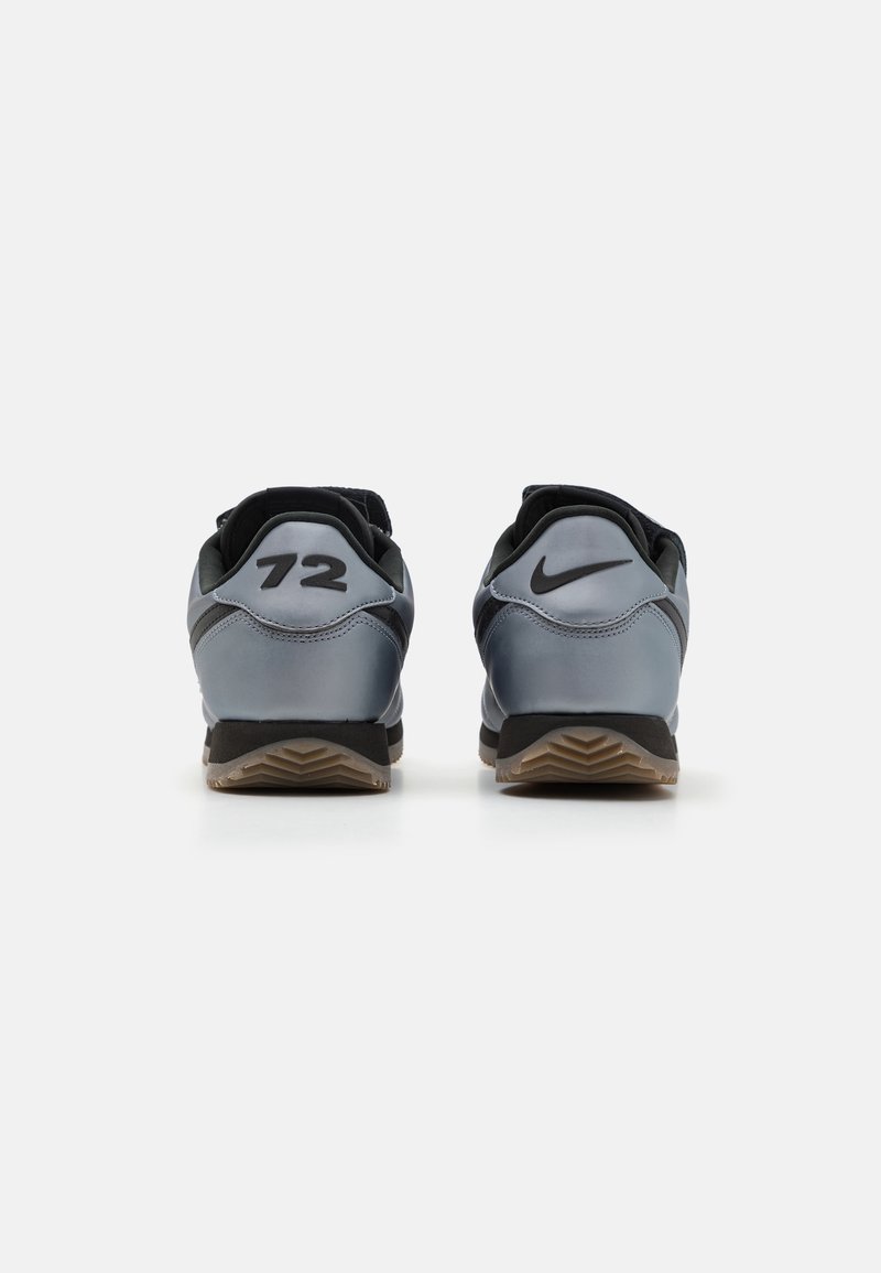 Zapatillas Nike con un diseño en gris y negro; presentan un destacado "72" negro y el logo en el talón, textura suave, suela de goma con un patrón de tracción.