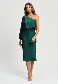 Satenasta obleka v smaragdno zeleni barvi z enim dolgim rokavom, volančastim izrezom in dolžino do kolen. Gladka tekstura; minimalističen dizajn.