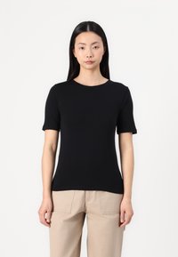 Top corto nero a maniche corte con scollatura rotonda, realizzato in un tessuto liscio. Modello aderente, abbinato a pantaloni beige in uno stile rilassato.