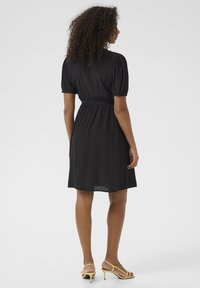 Robe noire à manches courtes avec une taille ajustée et une jupe évasée. Fabriquée en tissu léger, elle présente un design décontracté et une texture subtile.