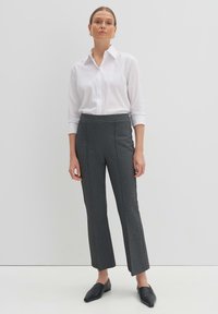 Pantalons cintrés gris avec une coupe évasée, détails de couture à l'avant, tissu texturé. Associés à une chemise blanche à col et des chaussures noires à enfiler.