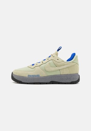 Sneakers con una toma in tessuto e suede verde chiaro, lacci blu e una suola in gomma nera testurizzata con accenti grigi e cuciture a zigzag.