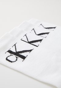 Fehér, bordás textúrájú zoknikat fekete "CK" logós szöveg díszíti, amely a zokni felső részén helyezkedik el.