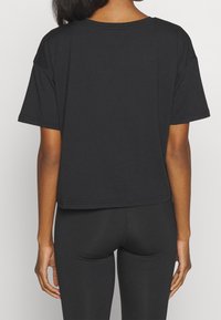 Camiseta corta negra de algodón, con mangas cortas, escote redondo y un corte relajado. Sin patrones ni adornos visibles.