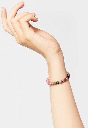 Kralenarmband met roze, zwarte en bruine stenen op elastiek, versierd met een accentkraal in kopertint. Hand gepositioneerd in een open gebaar.