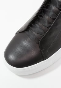 Sneaker in pelle nera con superficie liscia, dotata di lacci piatti e suola in gomma bianca. Il design include accenti minimalisti e nessun abbellimento.