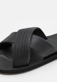 Svarta sandaler med två texturerade korskärningar. Tillverkade av syntetmaterial med en platt gummisula och subtil branding.