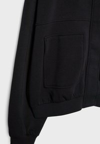 Črna mikica s zipper zapiranjem, dolgimi rokavi, rebrastimi manšeti in velikim sprednjim žepom z gladko teksturo.