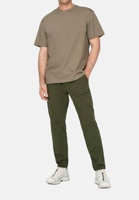 Khakifarbene Baumwoll-T-Shirt kombiniert mit grünen Hosen, im lässigen Schnitt. Weiße Sneakers runden das Outfit ab und betonen den lässigen Stil.