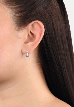 Orecchino a cerchio in argento mostrato su un orecchio, caratterizzato da una finitura liscia e un piccolo cristallo decorativo, che mette in risalto il suo design moderno.