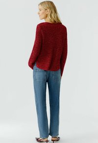 Roter strukturiertes Strickpullover mit lockerer Passform, runder Ausschnitt, seitlichen Schlitzen und kombiniert mit hellblauen, geraden Jeans.