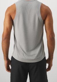 Graues ärmelloses Tanktop mit glatter Textur, rundem Ausschnitt und genähtem Saum. Getragen mit dunklen Shorts, die ein minimalistisches Design zeigen.