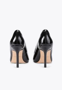 Czarne lakierowane szpilki z wyostrzonym noskiem, gładką teksturą i smukłym obcasem w kształcie stiletto. Widoczne subtelne detale haftu.