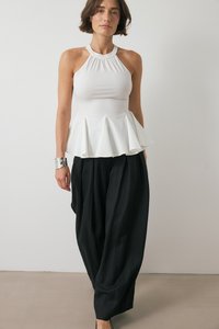 Hvid halterneck peplum top lavet af glat stof med rynket halsudskæring, parret med løse sorte bukser med tekstureret overflade.