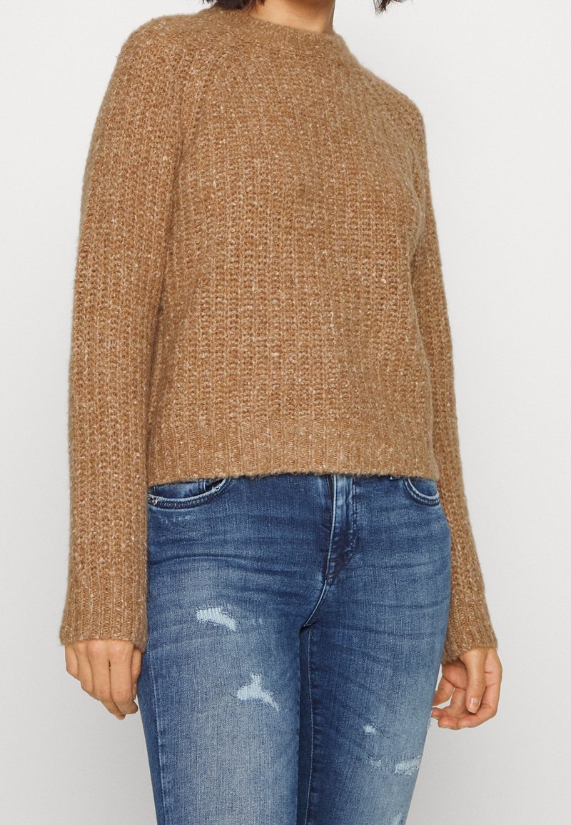 Brauner, gestrickter Pullover mit strukturiertem Finish, Rundhalsausschnitt und langen Ärmeln, kombiniert mit ausgewaschenen blauen Jeans.