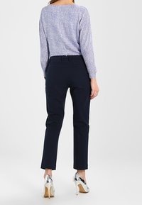 Marinblå skräddarsydda byxor med smal passform, kombinerade med en texturerad ljuslila långärmad topp och silverfärgade högklackade skor.