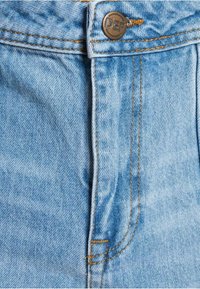 Lys blå denim jeans har en lynlås, en metal knap med "DEF" og kontrastfarvet orange syninger langs sømmene.