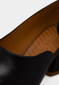 Μαύρο δερμάτινο παπούτσι με υφή στην επιφάνεια, με ανοιχτή φτέρνα και ταμπά εσωτερικό. Η σόλα έχει ανάγλυφο σχέδιο για καλύτερη πρόσφυση.