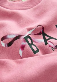Felpa rosa con una grafica raffigurante una lettera "B" nera, decorata con un nastro rosa e bianco. Tessuto in cotone testurizzato.