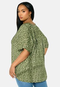 Grönmönstrad blus med korta ärmar, med en botanisk design, samlad halsringning och avslappnad passform. Matchad med ljusblå jeans.