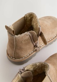 Bottines en daim beige à motif avec doublure en shearling, fermeture éclair latérale et détail cousu le long de la semelle. Tissu texturé et intérieur doux pour le confort.