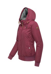 Veste bourgogne avec une capuche doublée de fourrure, fermeture zippée sur le devant et poignets élastiques. Présente des accents en bois et des poches latérales. Texture douce.
