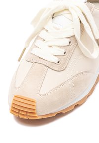 Sneaker beige con tomaia in suede e tessuto, lacci bianchi piatti e suola in gomma arancione. Presenta dettagli cuciti ed occhielli metallici.