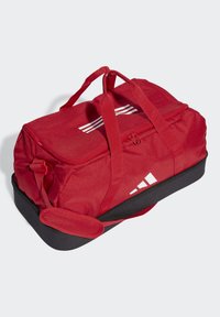 Bolsa de deporte roja con base negra, dos asas de transporte, cierre de cremallera, tres rayas blancas en la parte superior y un logo blanco en el lateral.