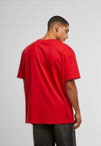 Camiseta de algodón roja, cuello redondo, mangas cortas, corte relajado, con una textura suave y sin patrones ni acentos visibles, presentada desde la parte posterior.