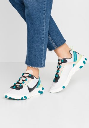 Witte en turquoise atletieksneakers met zwarte veters gedragen met blauwe spijkerbroek, met een zij- en vooraanzicht van de schoenen in een looppositie.
